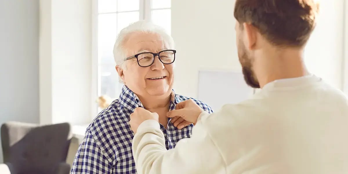 Mann knöpft Senior das Hemd zu