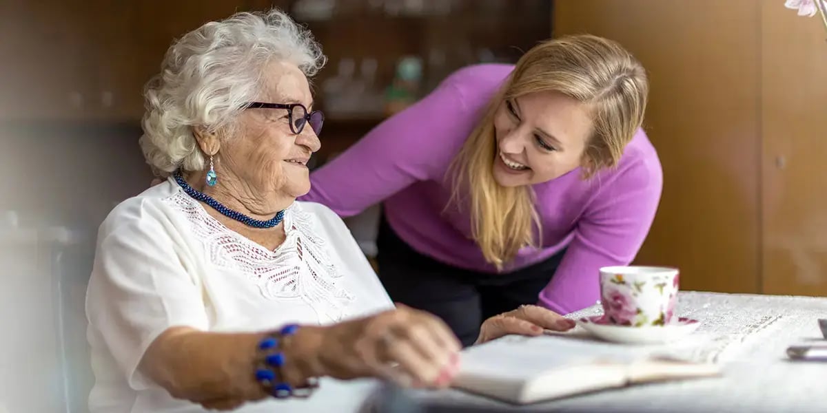 24-Stunden-Betreuerin beugt sich zu Seniorin