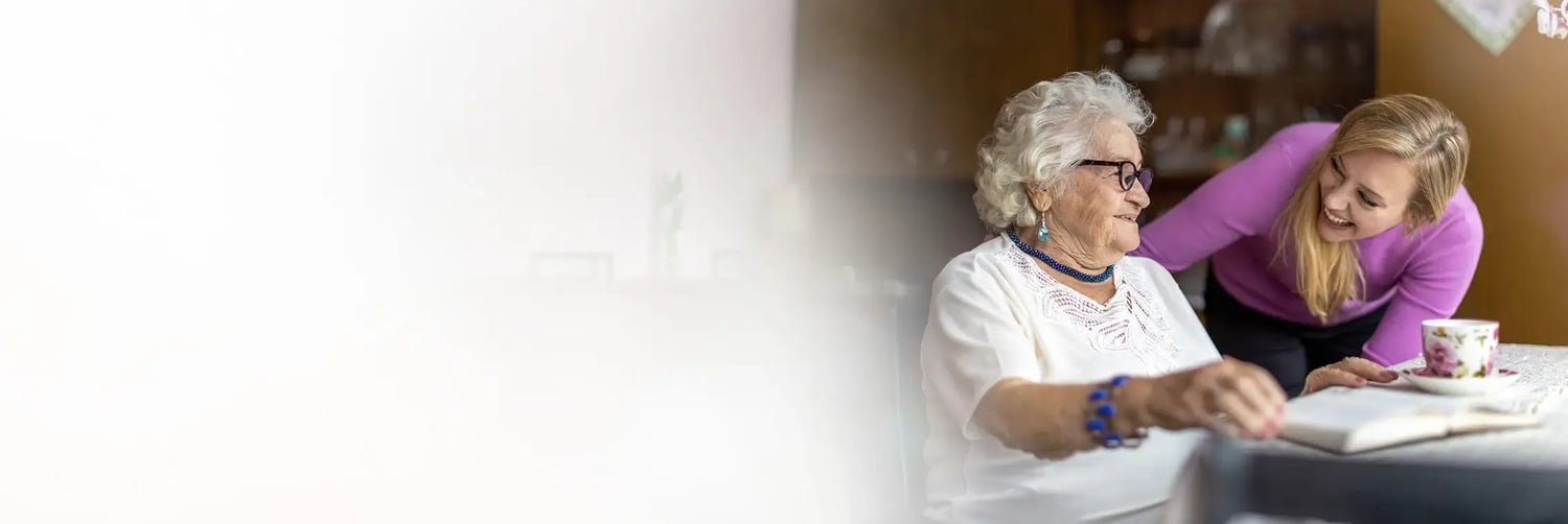 24-Stunden-Betreuerin beugt sich zu Seniorin